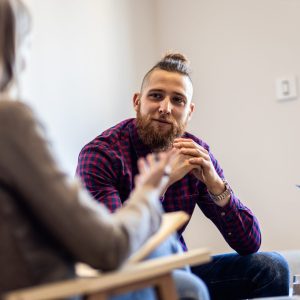 the photo shows a man sitting down and engaging in conversation with a female therapist