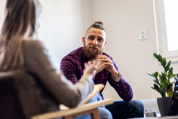 the photo shows a man sitting down and engaging in conversation with a female therapist