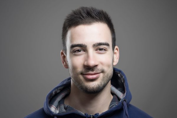 a young white man with short dark hair is smiling at the camera, he is also wearing a blue hoodie.