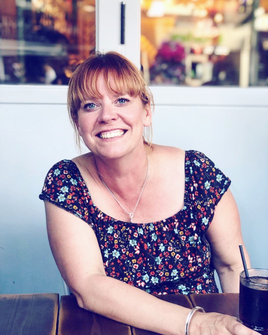 the photo shows our staff member Hilary, who is sitting down inside and smiling straight at the camera while holding a glass of coca cola