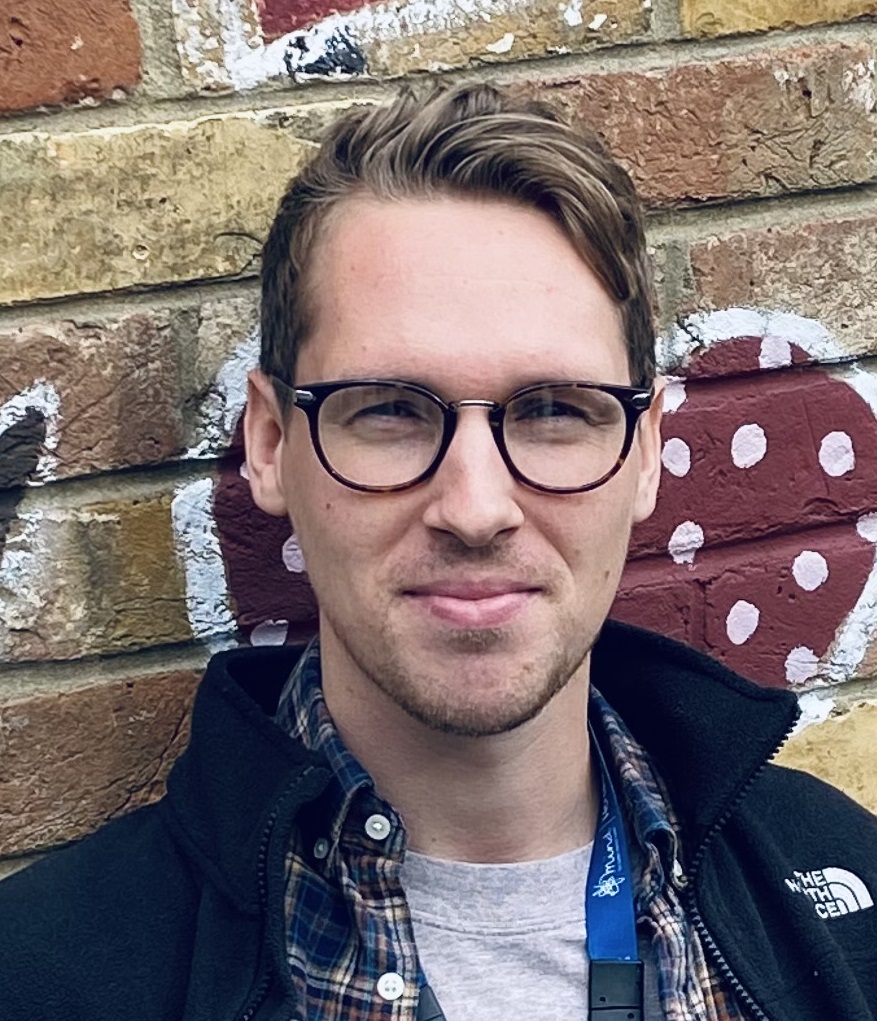 the photo shows our staff member Mike, who is in front of a brick wall, he is wearing glasses and looking at the camera with a slight smile