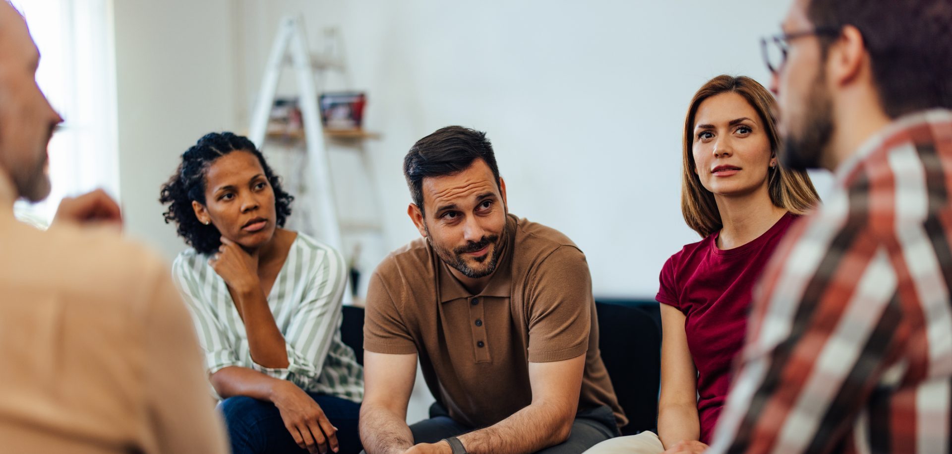 a group of people are sitting inside in a circle of chairs and are engaged in a discussion