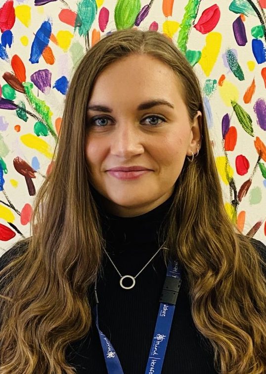 the photo shows our staff member Hannah, who has green eyes and long wavy hair, she is looking at the camera with a slight smile