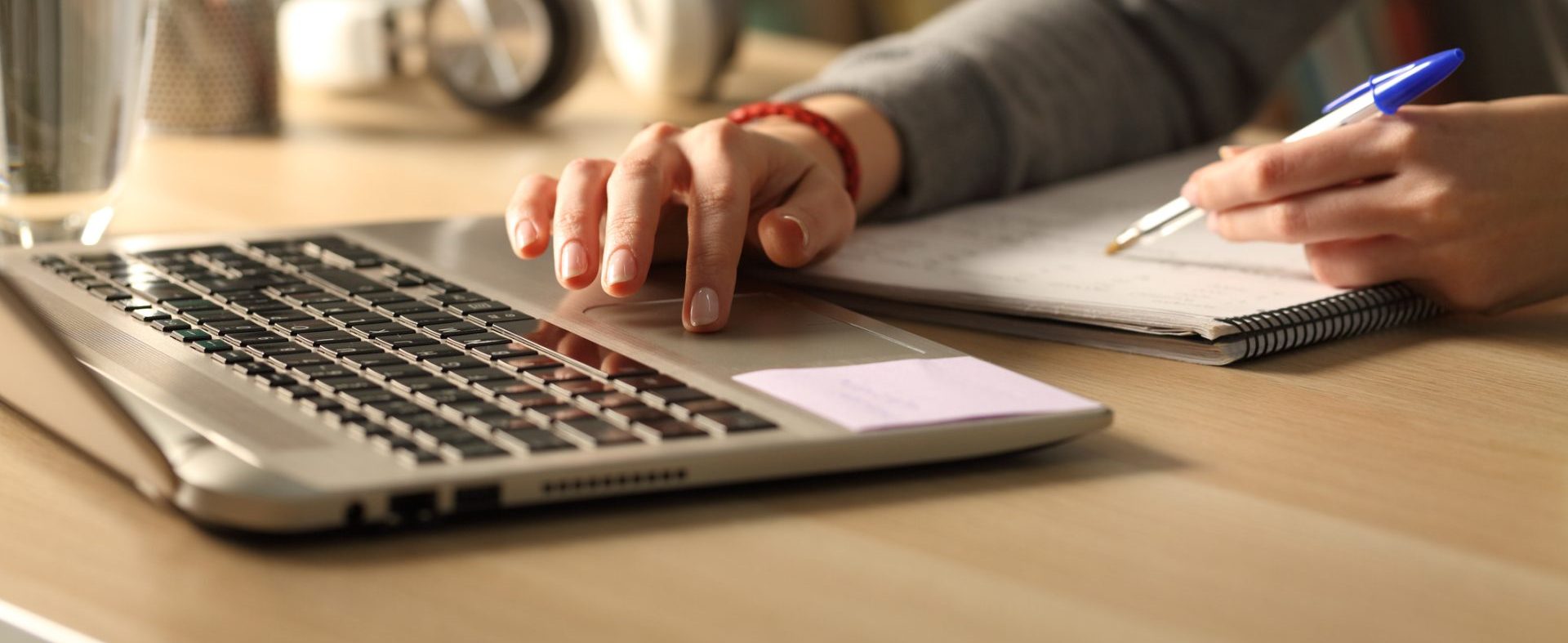 the image shows the keyboard of a laptop computer and someone's hand is using the mouse pad while writing notes in a book